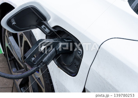 Charger is plugged into an electric car providing energy to the vehicle at a charging station in the morning light 139780253