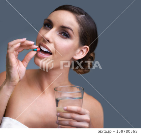 Woman, pill and water for healthcare, medication or drugs on a blue studio background. Female person. brunette or model with antibiotic, pharmaceuticals or vitamin supplement for wellness on mockup 139780365