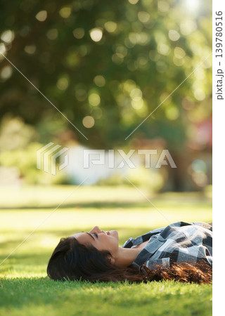Happy, park and woman on grass to relax for rest in garden, nature or field with smile or peace. Smile, freedom and female person on break with smile on face for summer vacation, holiday or wellness 139780516