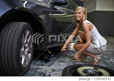 Woman, car jack and change tyre for maintenance in parking garage for breakdown or wheel failure, puncture or service. Female person, fashion and tools for transportation fix or repair, auto or lift 139780541