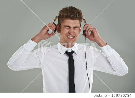 Businessman, headphones and stress for music or audio, streaming radio and song on gray background. Male person, anxiety and listening to playlist or podcast, overwhelmed and frustrated with sound 139780754