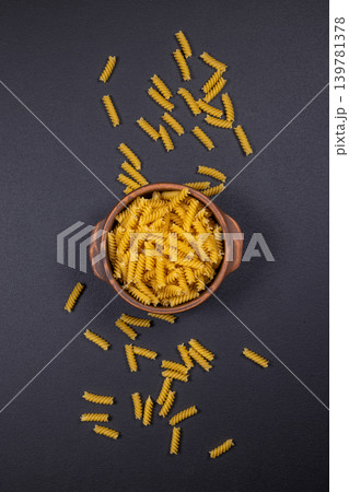 Dry fusilli pasta filling terracotta bowl on dark background Dry fusilli pasta filling terracotta bowl on dark background 139781378