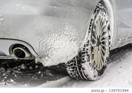 Snow covered rear wheel tire of silver car standing on winter ground, closeup detail Snow covered rear wheel tire of silver car standing on winter ground, closeup detail 139781994