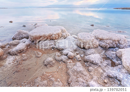 Sand and stones covered with crystalline salt on shore of Dead Sea, clear water background - typical morning scenery at Ein Bokek beach, Israel Sand and stones covered with crystalline salt on shore of Dead Sea, clear water background - typical morning scenery at Ein Bokek beach, Israel 139782051