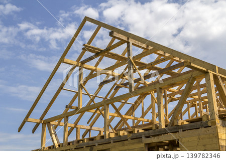 New wooden ecological house from natural materials under construction. Close-up detail of attic roof frame against clear sky. Building, roofing, construction and renovation concept. New wooden ecological house from natural materials under construction. Close-up detail of attic roof frame against clear sky. Building, roofing, construction and renovation concept. 139782346