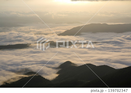 Fantastic view of mountain valley covered with low white puffy like snow clouds stretching to foggy horizon under bright morning sky with light orange glow at sunrise. Beauty of nature concept. Fantastic view of mountain valley covered with low white puffy like snow clouds stretching to foggy horizon under bright morning sky with light orange glow at sunrise. Beauty of nature concept. 139782347