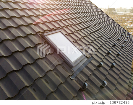 Close-up of new attic plastic window installed in shingled house roof. Professionally done building and construction work, roofing and installation concept. 139782453