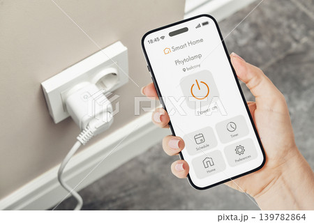 Female hand holding smartphone with smart home application interface for controlling a smart socket 139782864