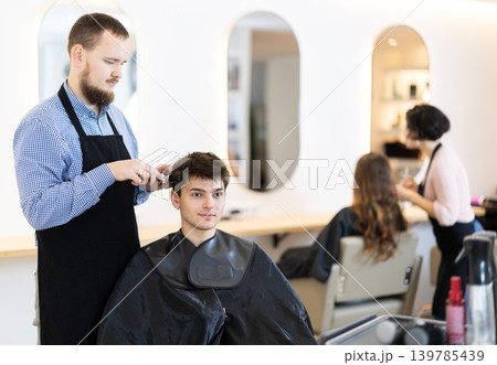 Young man barbershop employee stands next to male client, discussing details of haircut 139785439