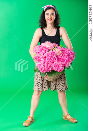 Portrait of positive adult woman with basket of pink flowers on green background. Chroma key compositing 139785467