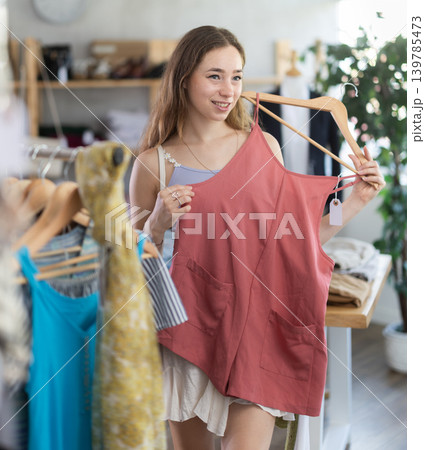 Woman chooses a set of clothes for the summer. Visitor to boutique examines the new summer collection of clothes Woman chooses a set of clothes for the summer. Visitor to boutique examines the new summer collection of clothes 139785473