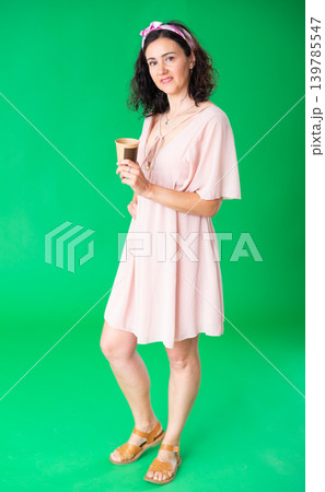 Woman in pink dress drinking coffee against a green chroma key background. Chroma key compositing. 139785547