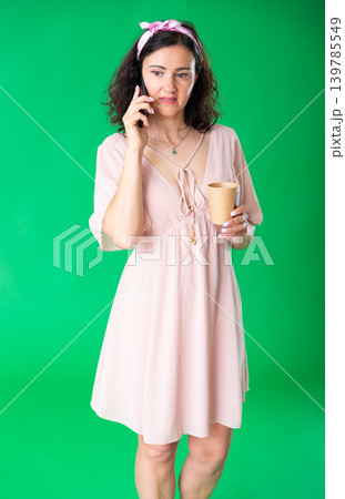 Adult woman with a cup of coffee talking on the phone on green background. Chroma key compositing. Adult woman with a cup of coffee talking on the phone on green background. Chroma key compositing. 139785549