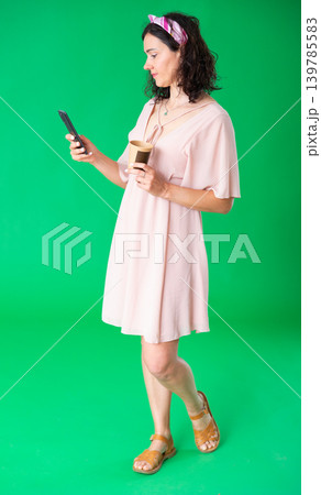 Woman in ping dress scrolling through her smartphone screen against and drinking coffee green screen background. Chroma key compositing Woman in ping dress scrolling through her smartphone screen against and drinking coffee green screen background. Chroma key compositing 139785583