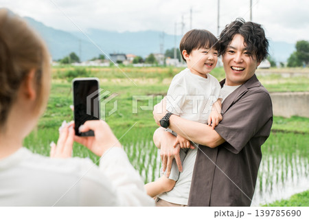 外で遊ぶ親子,子どもとパパの写真をスマホで撮るママ 139785690
