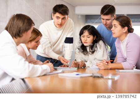 Group of girls and boys studying in classroom school, sitting around desks and attending teacher lecture Group of girls and boys studying in classroom school, sitting around desks and attending teacher lecture 139785742