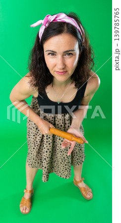 Emotional woman with rolling pin in hands screaming and expressing emotions on green background 139785765