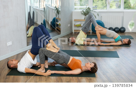 Lovers of active lifestyle perform pair yoga bridge and supported shoulderstand pose in gym Lovers of active lifestyle perform pair yoga bridge and supported shoulderstand pose in gym 139785834