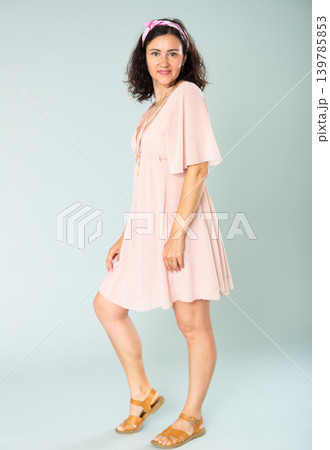 Portrait of cheerful adult woman in pink dress on gray background 139785853