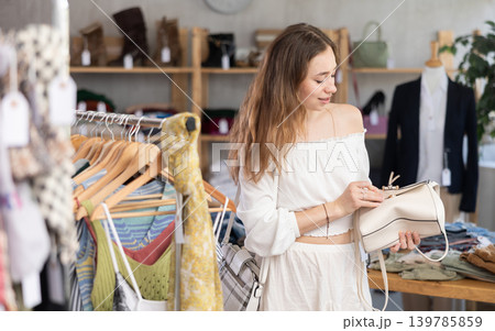 Happy young woman choosing handbag in clothing store Happy young woman choosing handbag in clothing store 139785859