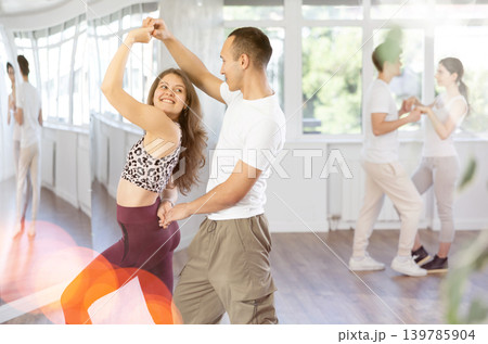 Young couple performs an expressive salsa in bright, modern dance studio during group class Young couple performs an expressive salsa in bright, modern dance studio during group class 139785904
