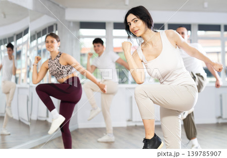 Positive woman and man engaged in dancing in group practices energetic swing in dance studio Positive woman and man engaged in dancing in group practices energetic swing in dance studio 139785907