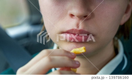 Close-up of young girl holding a piece of fried potato snack while seated in a car, with soft focus on the background Close-up of young girl holding a piece of fried potato snack while seated in a car, with soft focus on the background 139786160