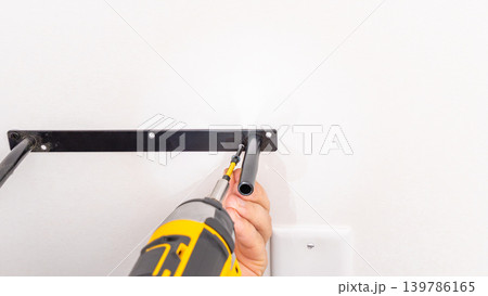 Mans hands aligning black metal shelf bracket on white wall during installation. Home improvement, bracket adjustment, DIY precise placement, mounting process. 139786165