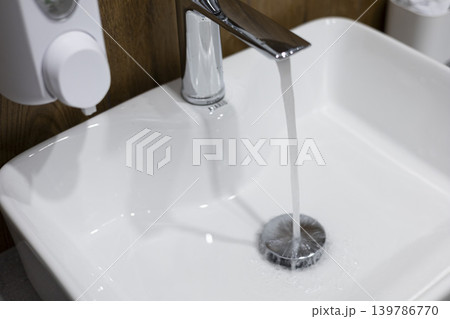 Water flowing from the tap into a clean white sink. Water flowing from the tap into a clean white sink. 139786770