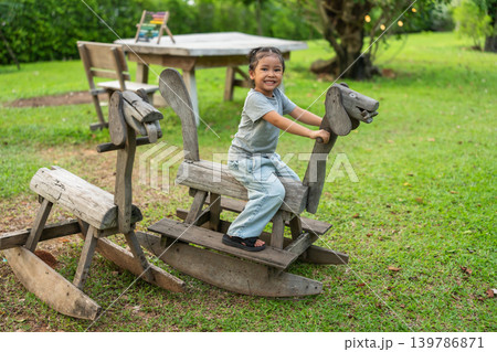 happy preschool child girl playing on wooden rocking horse in outdoor playground happy preschool child girl playing on wooden rocking horse in outdoor playground 139786871