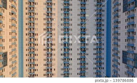 High-angle view of a modern high-rise residential apartment building with blue balconies and a swimming pool at the base during golden hour. High-angle view of a modern high-rise residential apartment building with blue balconies and a swimming pool at the base during golden hour. 139786886