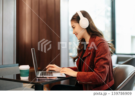 professional Asian woman wears headphones while working on her laptop at a modern cafe, representing online education, remote meetings professional Asian woman wears headphones while working on her laptop at a modern cafe, representing online education, remote meetings 139786909