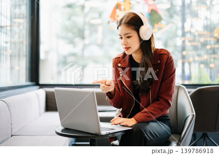 young Asian freelancer works on her laptop in a modern cafe, representing remote work, digital nomad lifestyle, and professional success in a casual setting. 139786918