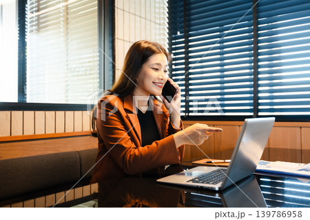 Asian businesswoman writing notes while working on laptop in modern office. Asian businesswoman writing notes while working on laptop in modern office. 139786958