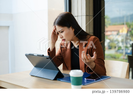 Stressed Asian businesswoman thinking at laptop in modern office. Professional female facing work pressure, problem solving Stressed Asian businesswoman thinking at laptop in modern office. Professional female facing work pressure, problem solving 139786980