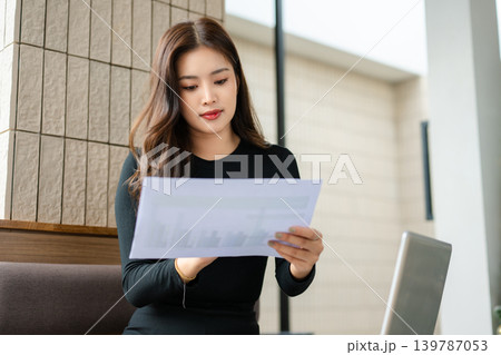 Asian businesswoman using laptop and smartphone while reviewing documents in a modern workspace, symbolizing productivity, remote work Asian businesswoman using laptop and smartphone while reviewing documents in a modern workspace, symbolizing productivity, remote work 139787053