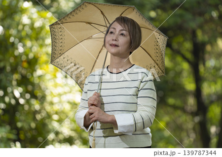 新緑の公園で日傘をさして散歩するシニア女性 139787344