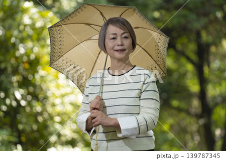 新緑の公園で日傘をさして散歩するシニア女性 139787345