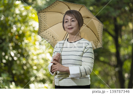 新緑の公園で日傘をさして散歩するシニア女性 139787346