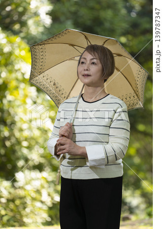 新緑の公園で日傘をさして散歩するシニア女性 139787347