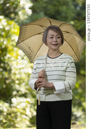 新緑の公園で日傘をさして散歩するシニア女性 139787350