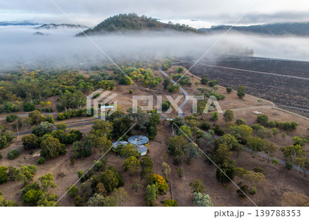 Aerial view of the Glenbawn Dam wall and surrounding landscape with fog rolling through the valley in NSW Australia. Drone photograph captures the reservoir, rugged mountain scenery and low cloud 139788353