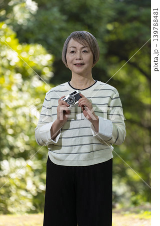 新緑の公園で趣味のカメラで写真を撮るシニア女性 新緑の公園で趣味のカメラで写真を撮るシニア女性 139788481