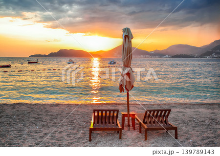 Amazing sunset at beach with chaise lounges and umbrellas in Sveti Stefan near Budva. Amazing sunset at beach with chaise lounges and umbrellas in Sveti Stefan near Budva. 139789143