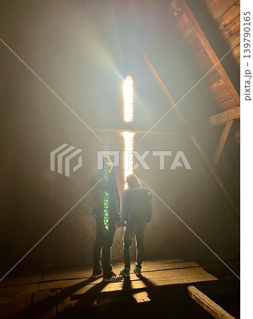 Two individuals standing in an attic illuminated by sunlight streaming through a Two individuals standing in an attic illuminated by sunlight streaming through a 139790165