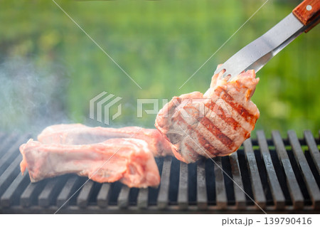 Pork steak grilling on barbecue with tongs outdoor close up Pork steak grilling on barbecue with tongs outdoor close up 139790416
