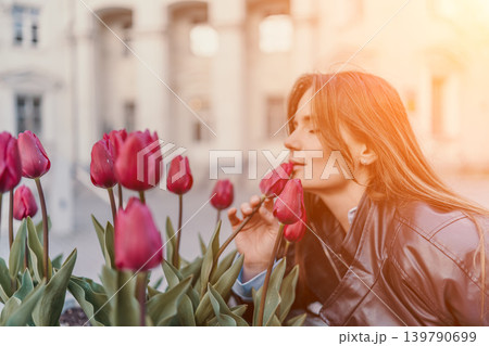 Woman tulip sunset serene young woman in a leather jacket smells vibrant red tulips in an urban garden at golden hour 139790699