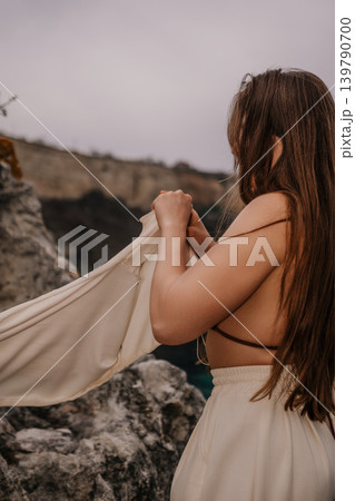 Woman cliff ocean standing on a rocky shore while holding a cream colored jacket under a moody overcast sky 139790700