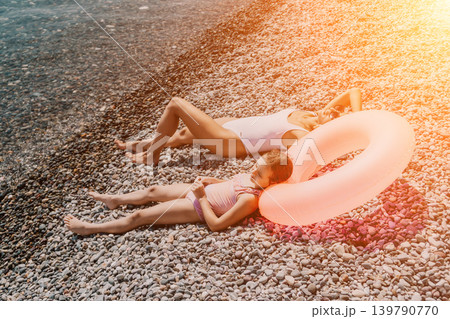 Beach vacation family lying on a sunny pebble shore with a pink inflatable ring enjoying summer holiday together 139790770