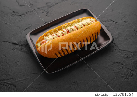 Hot dog served on a black plate with toppings at a restaurant Hot dog served on a black plate with toppings at a restaurant 139791354